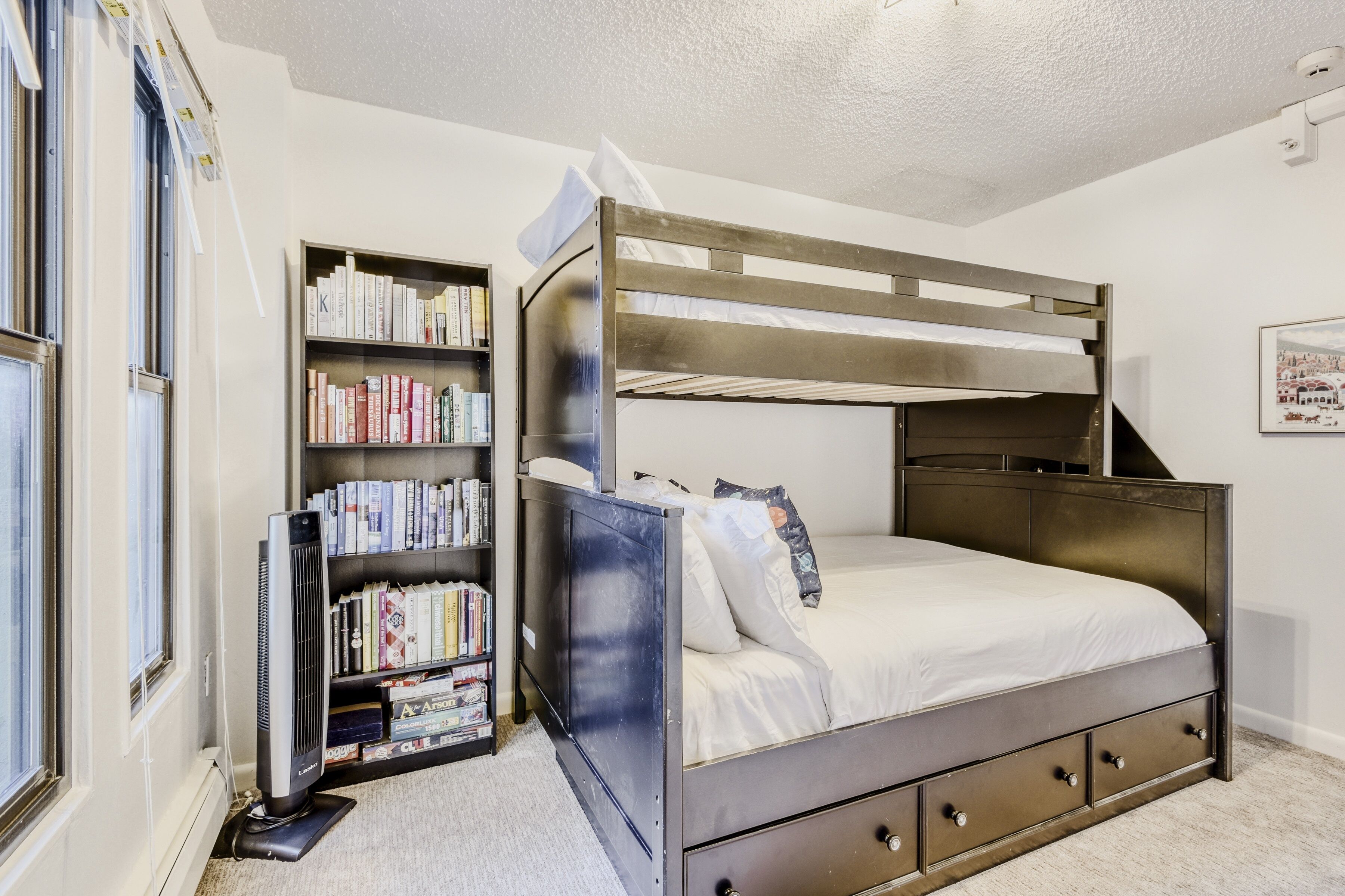 A bunk bed with a bookshelf beside it, a heater, and a window.