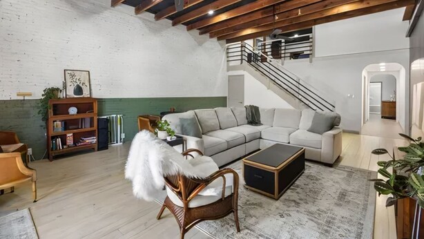 Ein geräumiges Wohnzimmer mit hoher Decke, sichtbaren Balken, einem großen Sofa, einem Couchtisch und einer Treppe, die in eine obere Ebene führt.