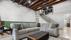 Ein modernes Wohnzimmer mit einem Ecksofa, einem schwarzen Couchtisch und einer Treppe, die in eine obere Ebene führt.
