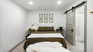 Ein modernes Schlafzimmer mit einem Bett, einer weißen Ziegelwand, drei gerahmten Blattform-Kunstwerken und einer Schiebetür zu einem Badezimmer.