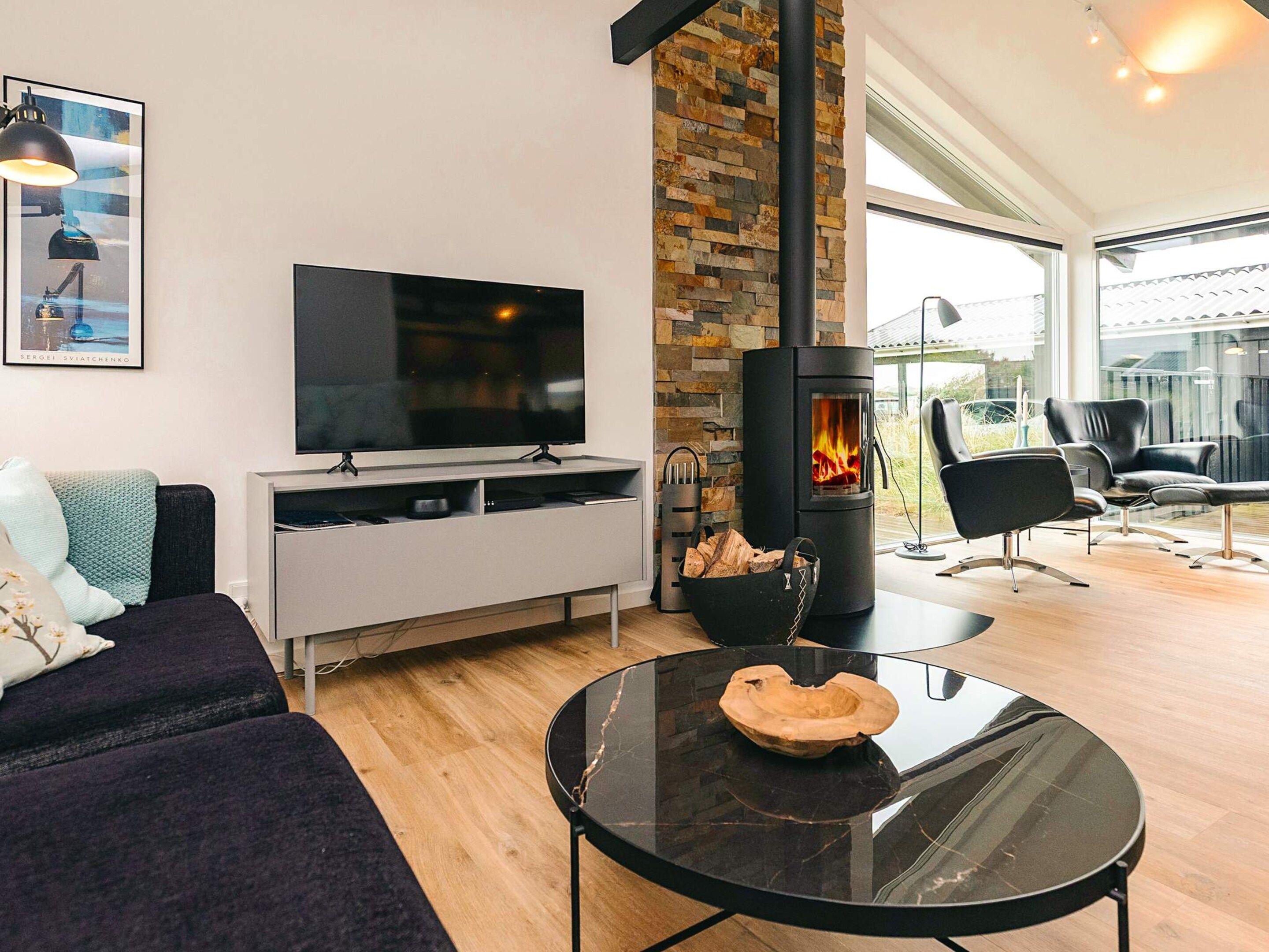 Una sala de estar moderna con un televisor de pantalla plana, una chimenea de piedra, un sofá y una mesa de centro de vidrio.
