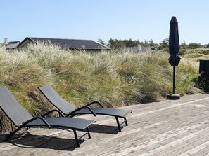 Eine Holzterrasse mit zwei Liegestühlen und einem Sonnenschirm.