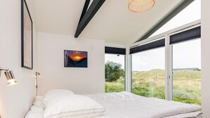Een moderne slaapkamer met een bed, een foto van een zonsondergang en grote ramen met uitzicht op de omgeving.