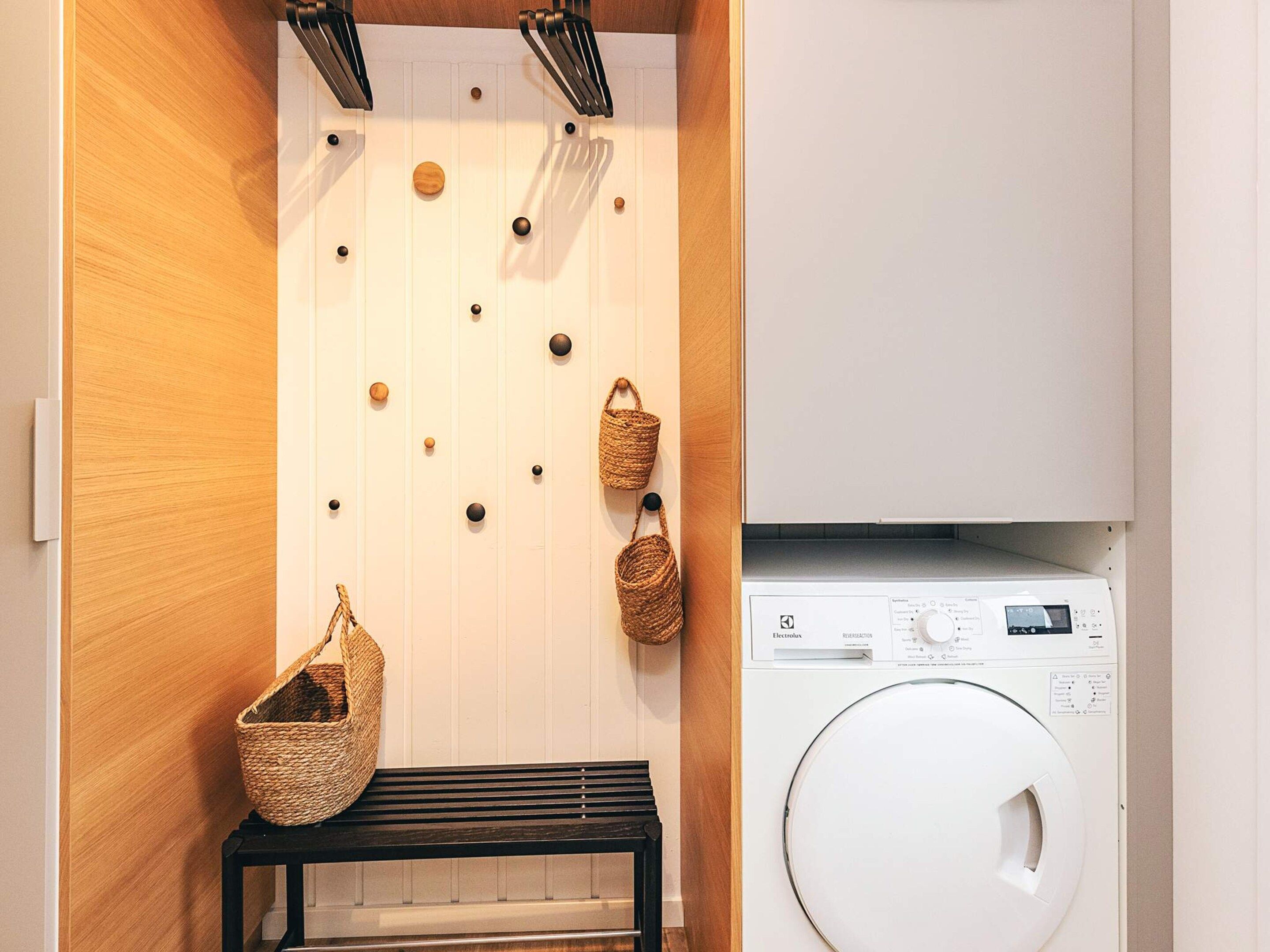 A laundry area with a washing machine, a bench, and wall-mounted baskets.
