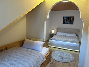 Une chambre avec deux lits, une petite table ronde et un tableau accroché au mur.