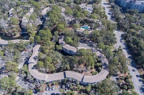 Vue aérienne d’un quartier résidentiel avec une route sinueuse, bordé d’arbres et comprenant une piscine.