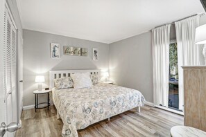 Une chambre à coucher avec un lit, des tables de chevet, une fenêtre avec des rideaux et des œuvres d’art accrochées au mur.