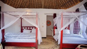 Una habitación con dos camas, cada una con dosel, suelo de madera y techo de paja.