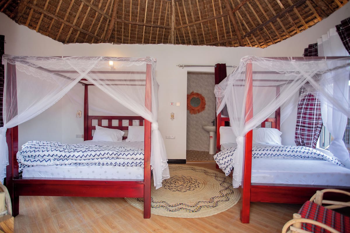 Ein Zimmer mit zwei Betten, jeweils mit Baldachin, Holzboden und einem Reetdach.