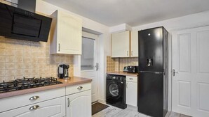 Cocina compacta con estufa a gas, lavadora y refrigerador negro.