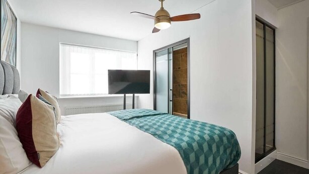 Un dormitorio con cama, ventilador de techo, televisión y puerta corrediza de cristal.