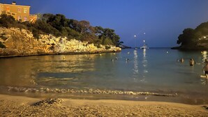 A coastal scene with a building on the left, calm water, and a boat in the distance. - Vacation home for families in Cala Ferrera with private pool in the garden near the beach (Cala Ferrera)