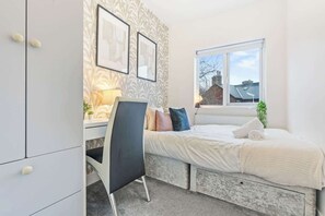 A bedroom with a bed, a desk, and a chair. There is a window with a view of buildings outside. - Stylish Spacious 3-Bed Sheffield Home (Highfield)