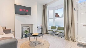 Ein modernes Wohnzimmer mit Flachbildfernseher, Kamin, Esstisch und Blick ins Freie.