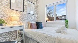 Ein Schlafzimmer mit einem Bett, einem Schreibtisch, einer Lampe und einem Fenster mit Blick nach draußen.