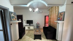 A living room with a TV, sofa, coffee table, and artwork on the walls. - NGK HOTEL APARTMENT (Bafoussam)
