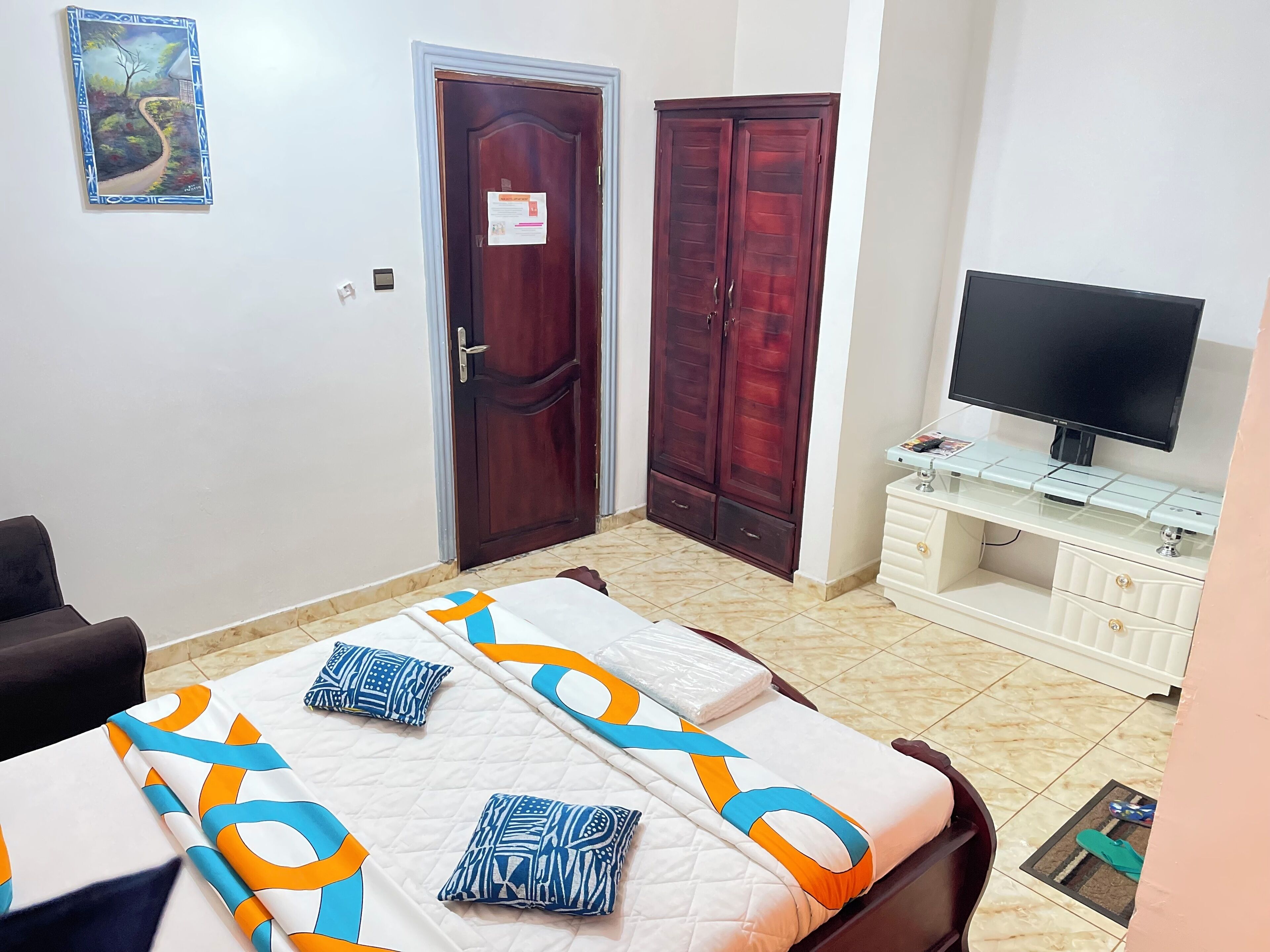 A bedroom with a bed, a TV, a wardrobe, and a painting on the wall.