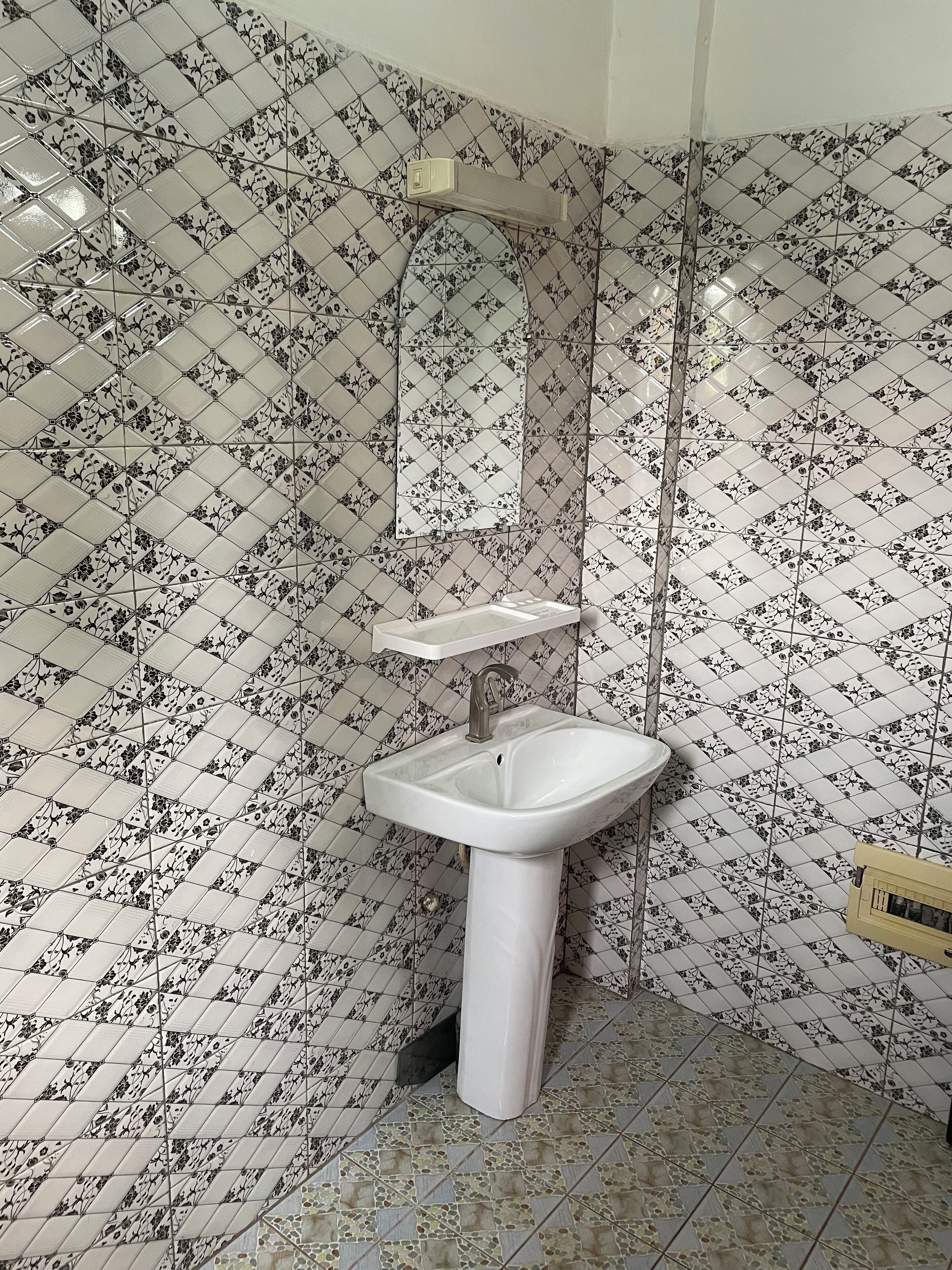 A bathroom with a white sink, a mirror above it, and patterned tiles on the walls and floor.