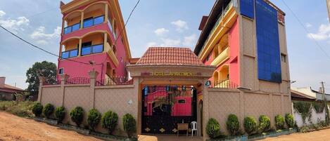 A multi-story hotel with a prominent entrance, a sign indicating it is an apartment hotel, and a small outdoor seating area.