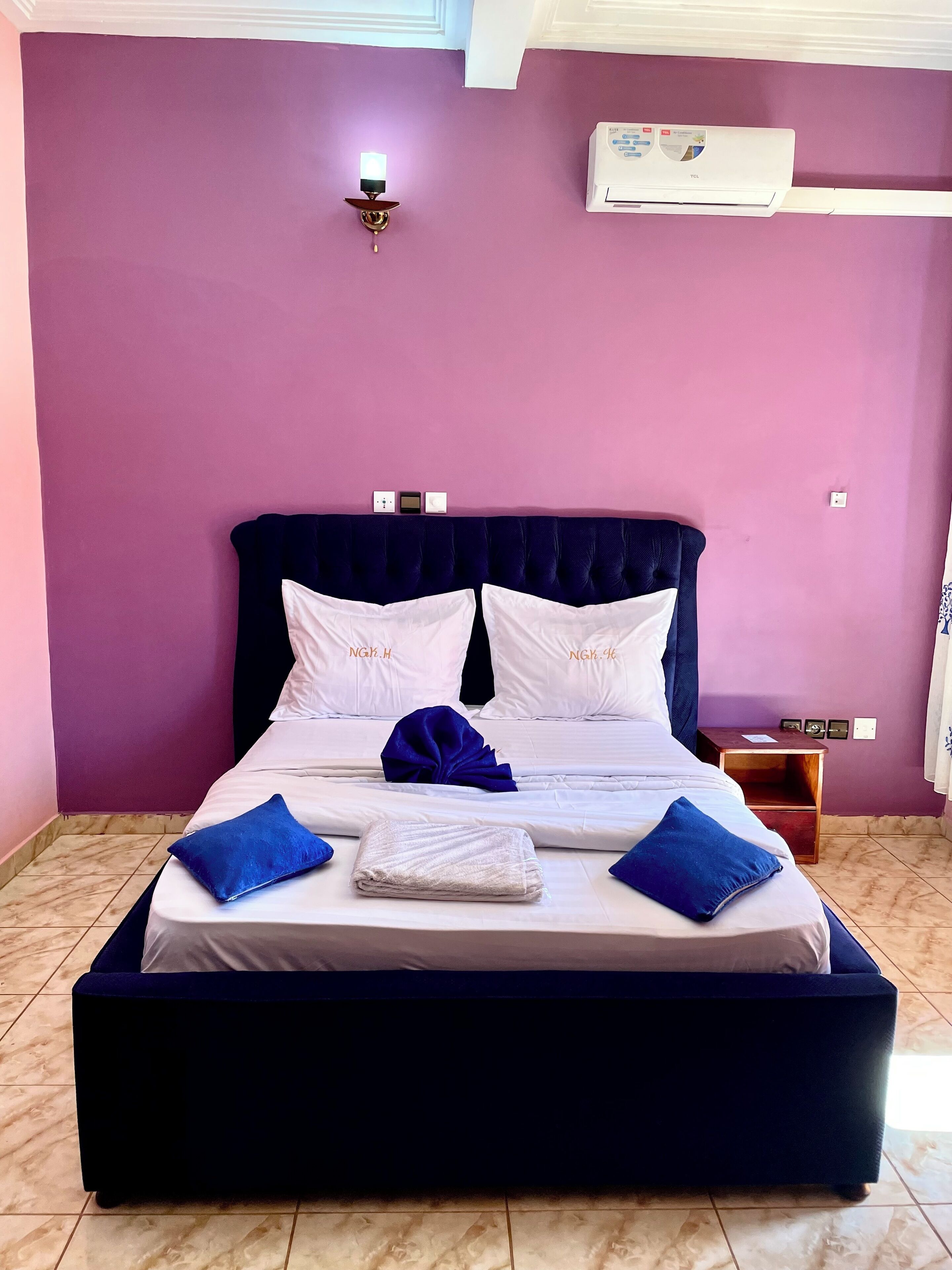A neatly made bed with white and blue pillows, a folded towel, and a blue throw blanket.