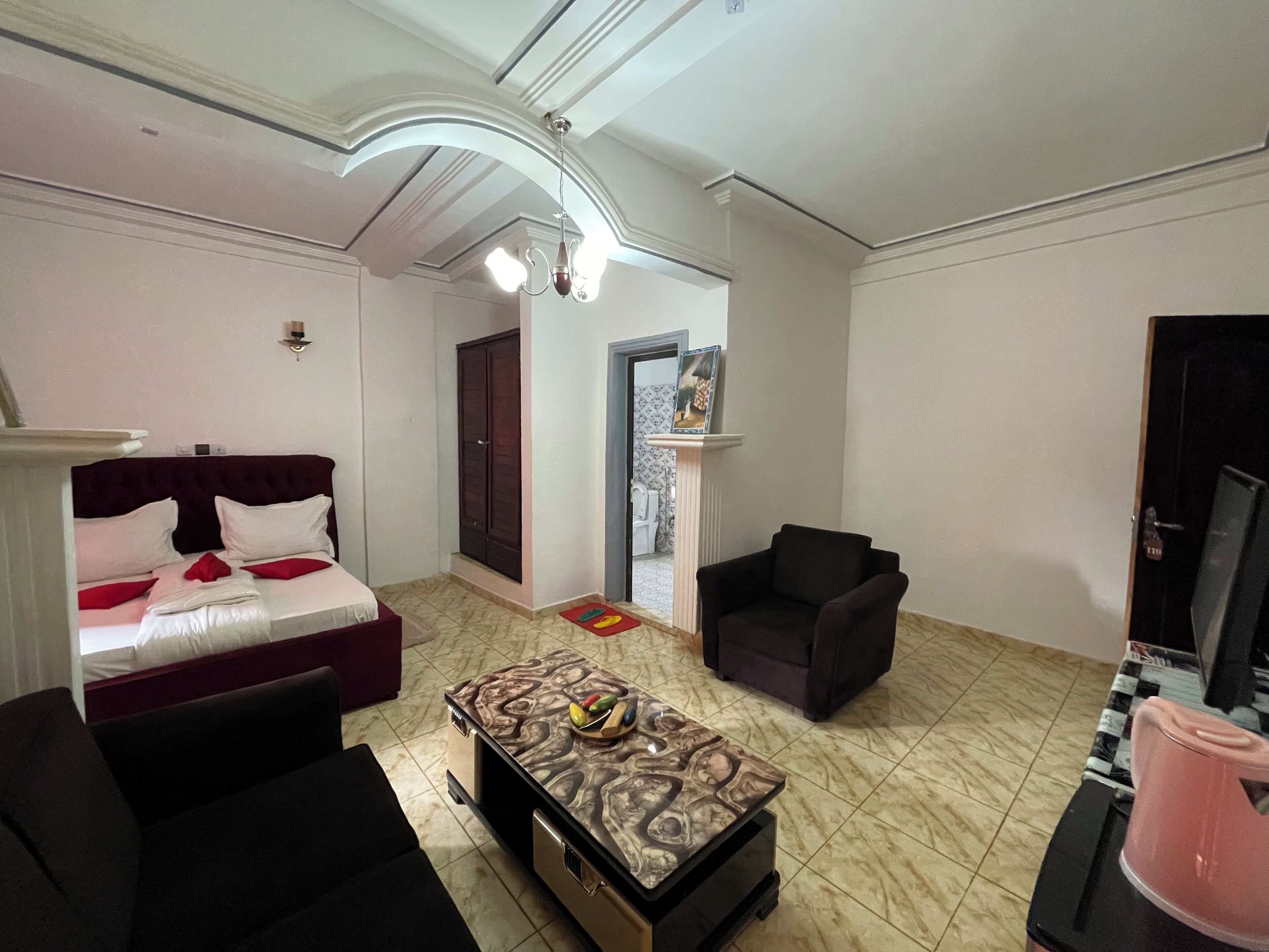 Een woonkamer met een bank, een bijzettafeltje met fruit, een televisie en een deur naar een andere kamer.