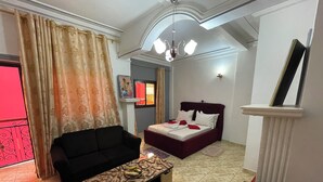 A compact hotel room with a bed, a sofa, a coffee table, and a small balcony. - NGK HOTEL APARTMENT (Bafoussam)