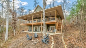 Une cabane à deux étages dotée d’un balcon, d’un espace extérieur aménagé pour s’asseoir et d’un sentier en pierre.