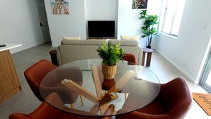 Un salon moderne avec une table à plateau en verre, des fauteuils en cuir, un canapé, un téléviseur et une plante en pot.