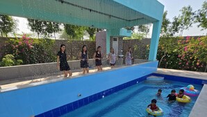 Une piscine où des enfants jouent, sous la surveillance d’adultes.