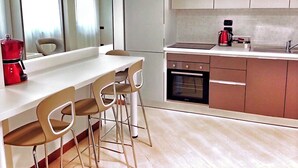 Une cuisine moderne avec un plan de travail blanc, deux tabourets de bar, une machine à café rouge et un four encastré.