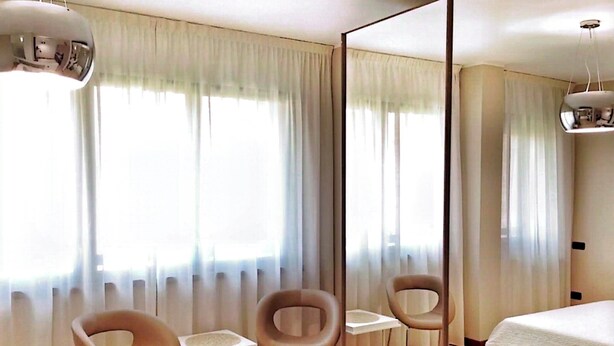 Une chambre d’hôtel moderne avec un grand lit, deux fauteuils, une petite table et un miroir.