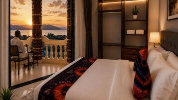 Habitación de hotel con una cama grande, una mesita de noche, un armario y un balcón con vistas al atardecer.