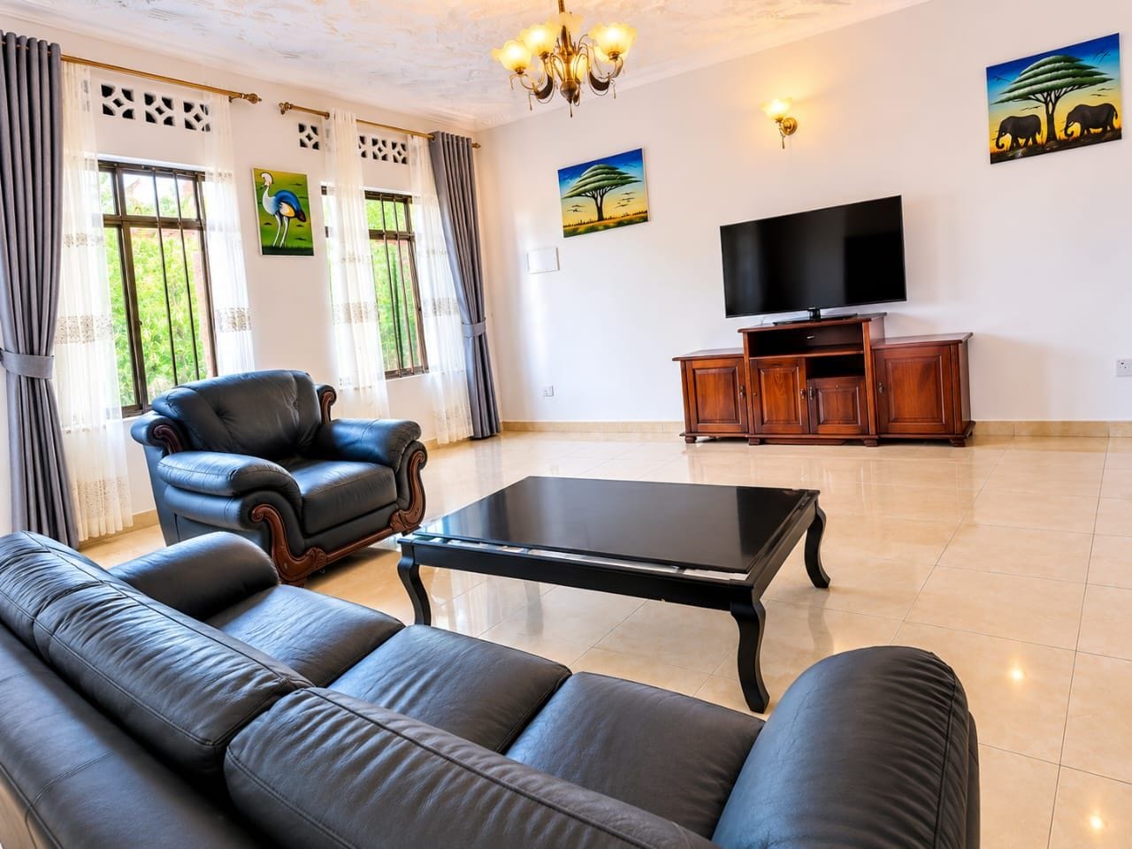 A living room with a sofa, a chair, a coffee table, a TV, and artwork on the walls.