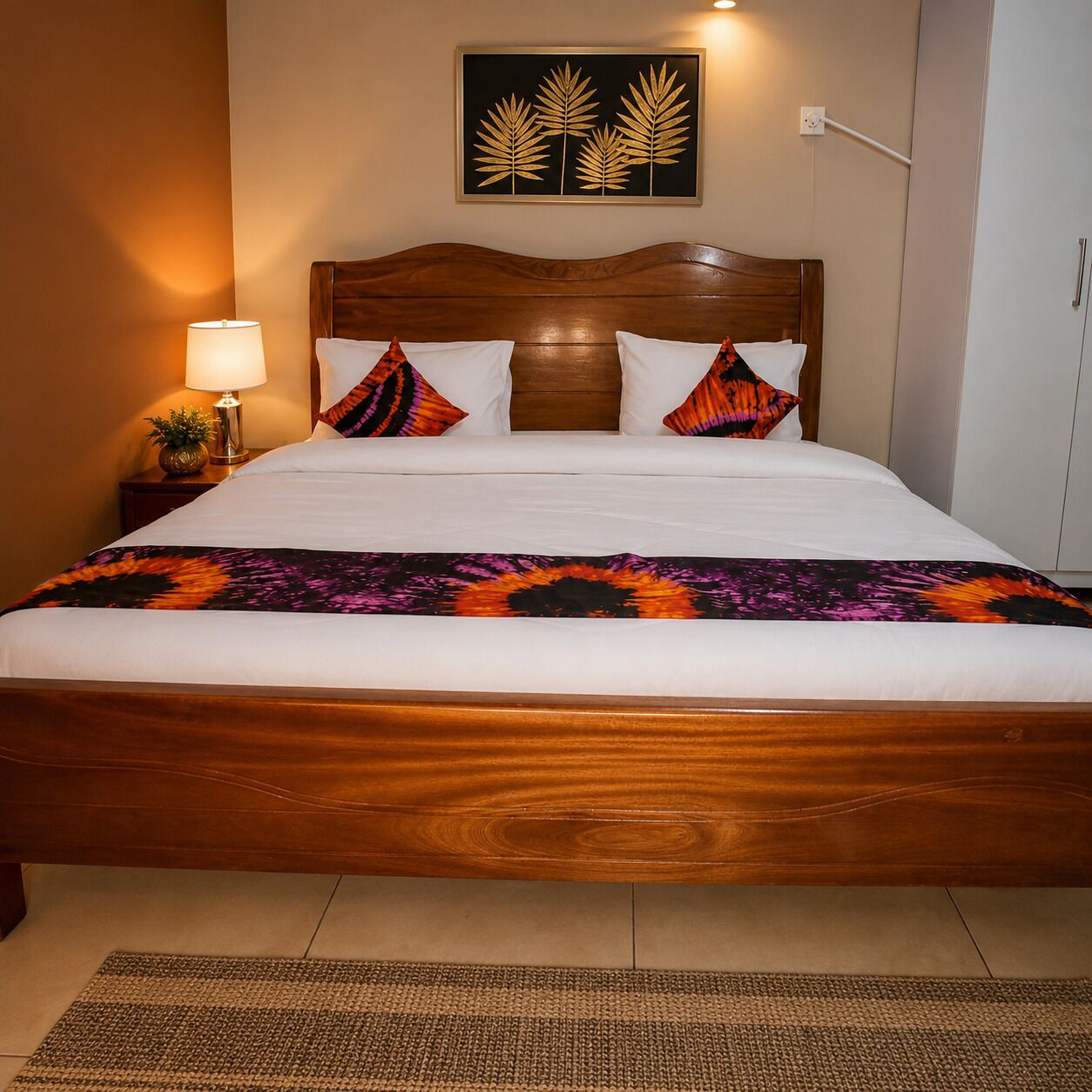 A hotel room with a wooden bed, white bedding, a patterned throw, and a wall-mounted artwork.