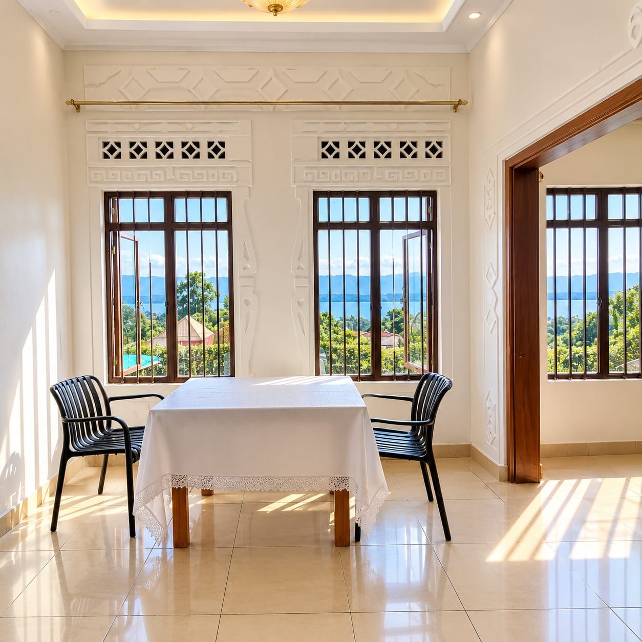 A room with a table and chairs, large windows with a view of greenery and water, and decorative wall patterns.