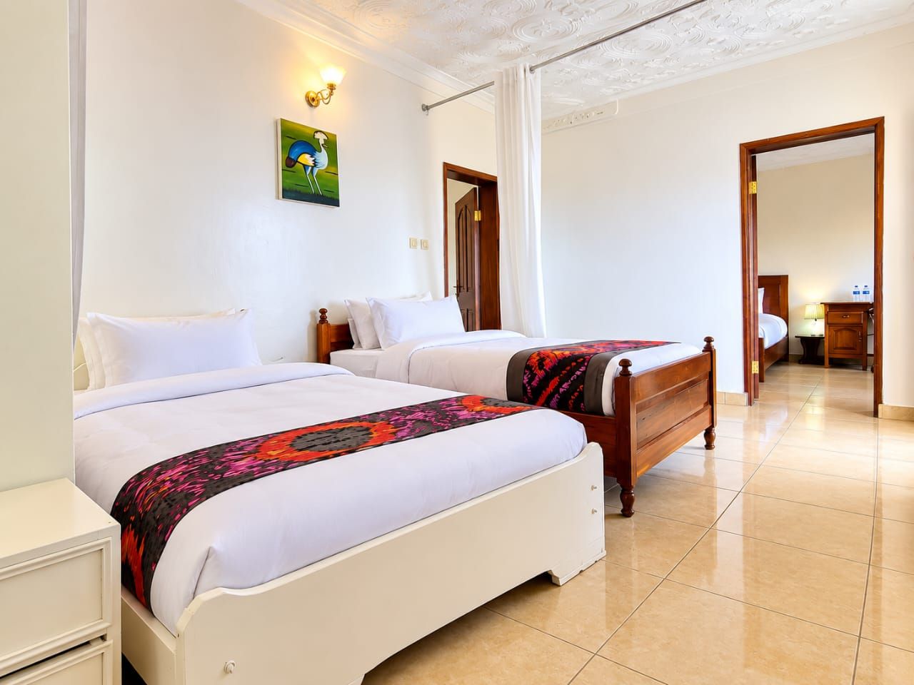 A hotel room with two beds, a wooden headboard, a painting on the wall, and a bathroom visible through an open door.