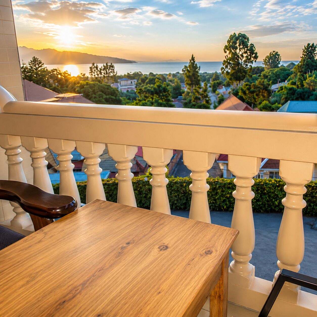 A wooden table and a chair on a balcony with a view of a body of water and trees.
