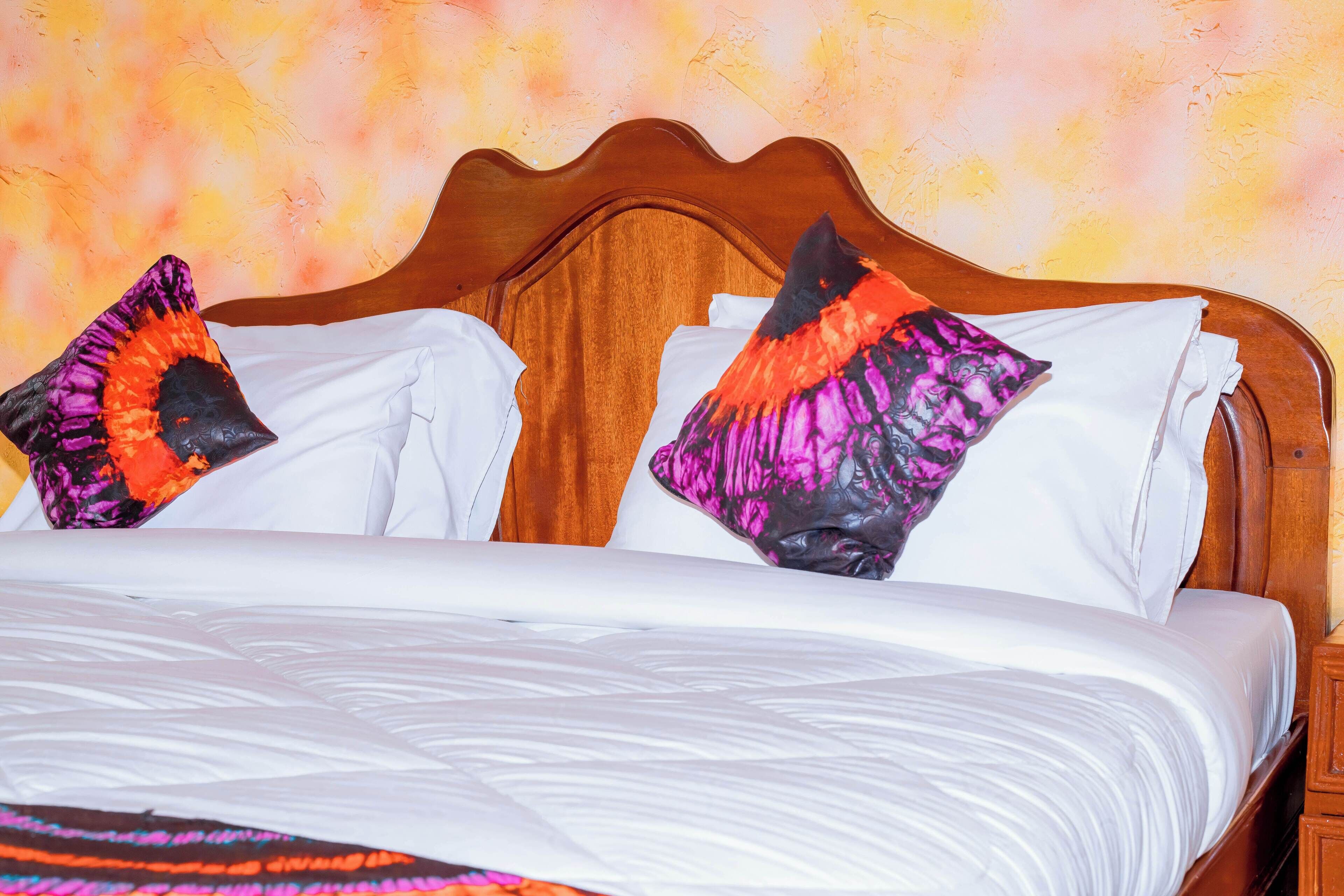 Una cama con ropa blanca y dos almohadas decorativas con estampado negro y naranja.
