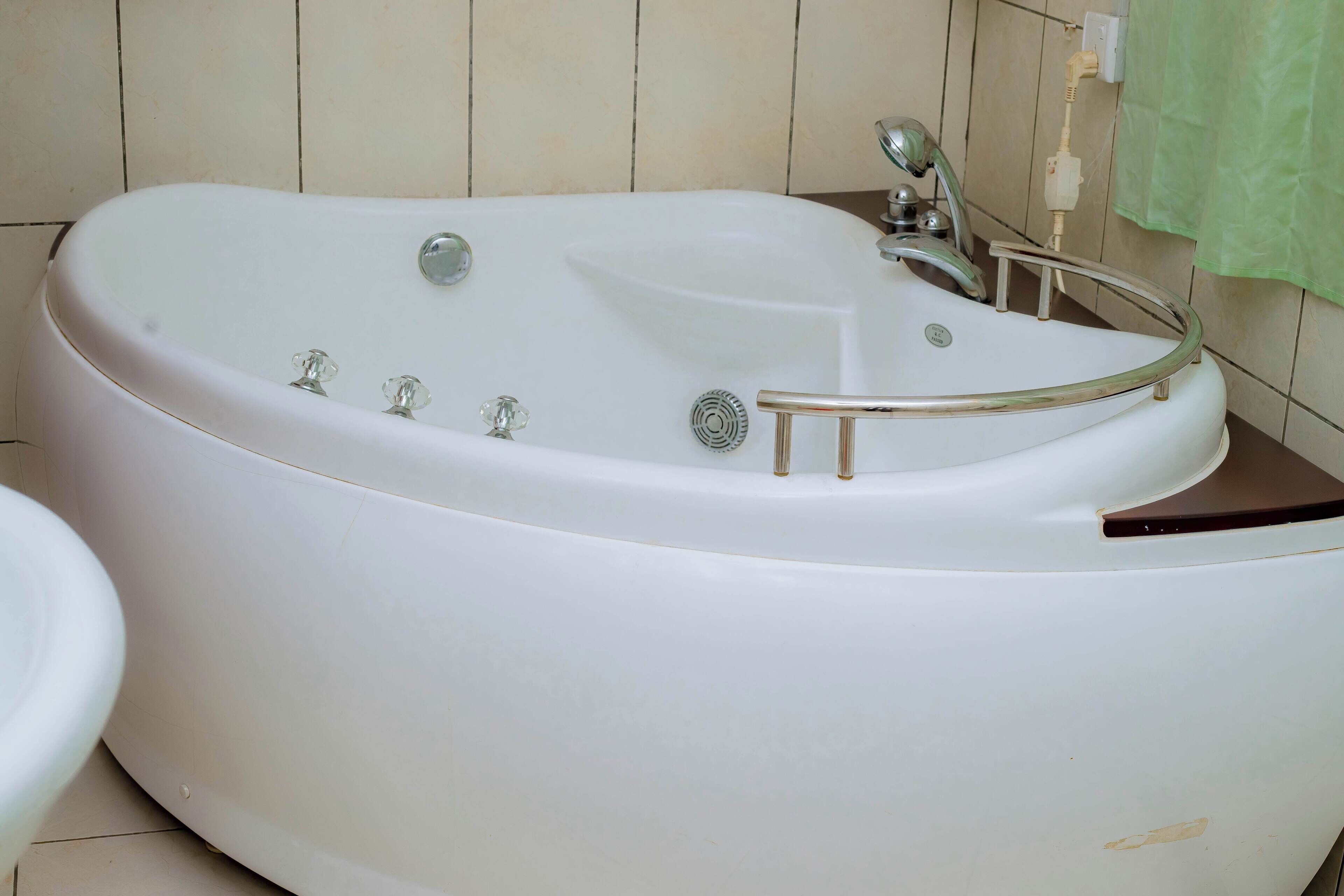 Una bañera blanca con puerta de vidrio, un cabezal de ducha manual y un rociador de ducha manual.