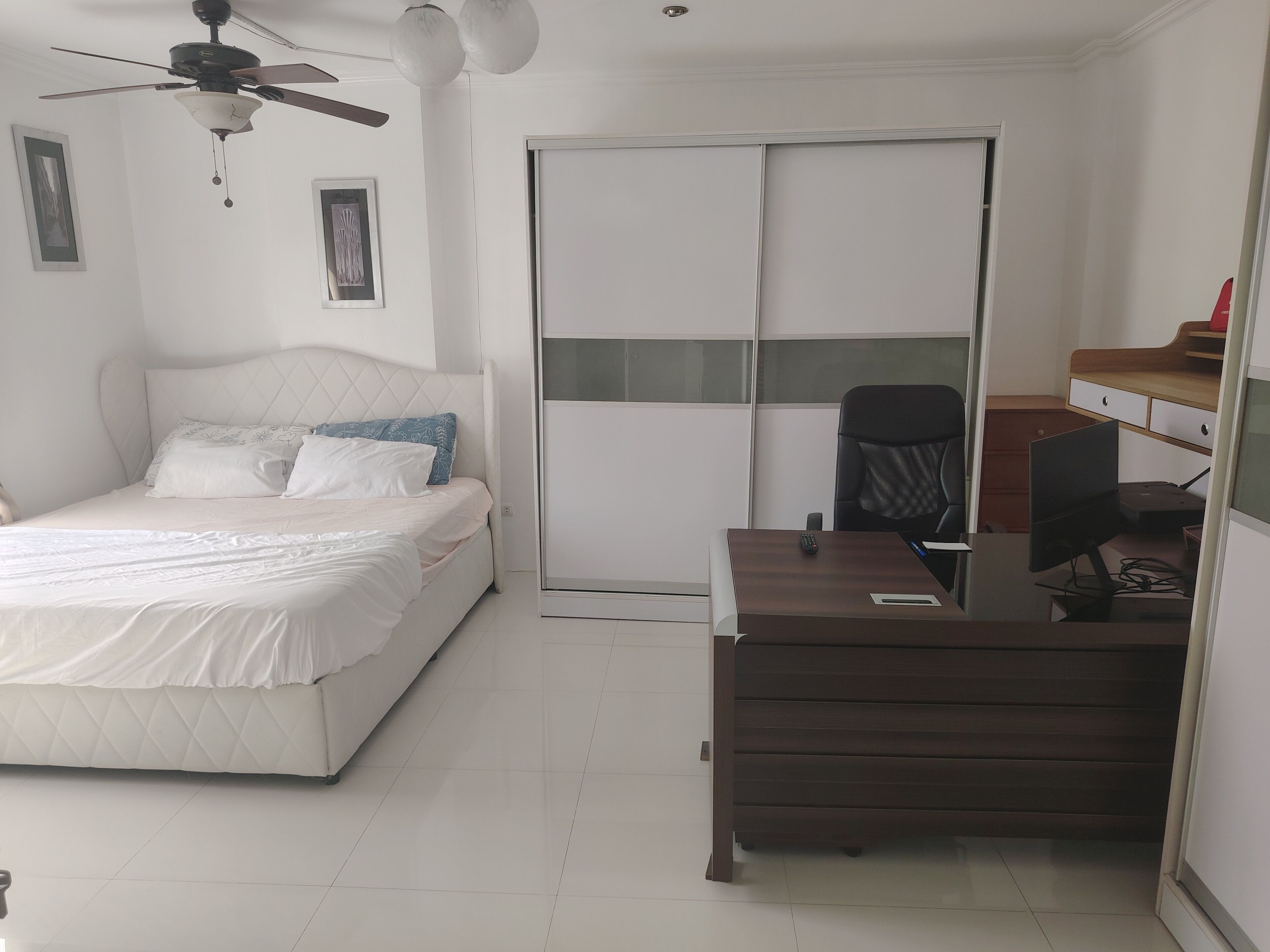 Ein Schlafzimmer mit Bett, Schreibtisch, Stuhl, Kleiderschrank und Deckenventilator.