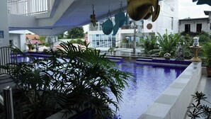 Une piscine intérieure avec vue sur les bâtiments environnants et un balcon agrémenté de décorations suspendues.