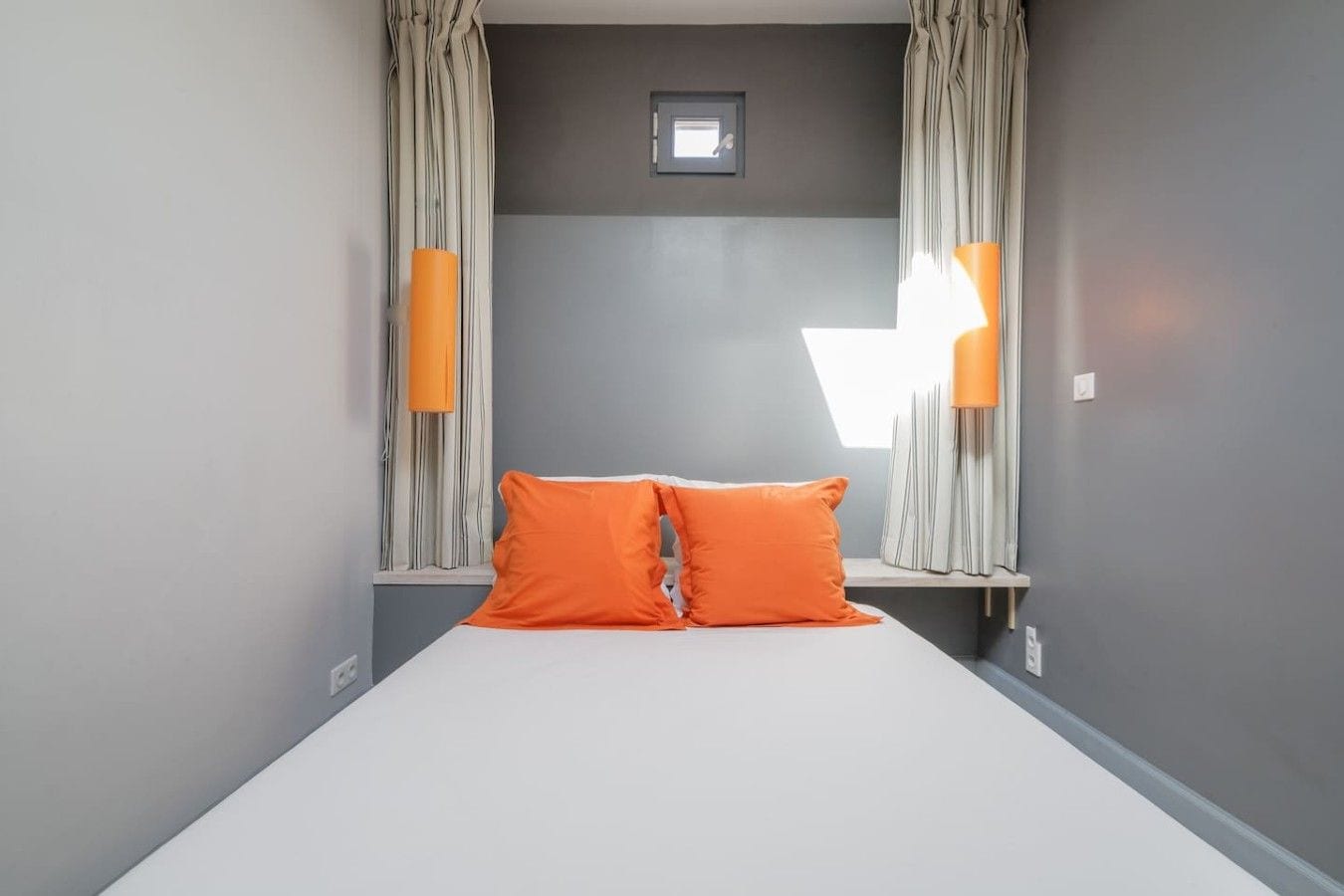 A hotel room with a bed, curtains, and two wall-mounted lamps.