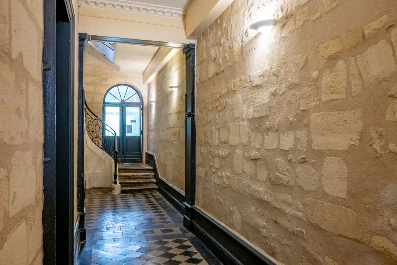 Un couloir avec un sol à carreaux, un escalier et un mur en pierre.