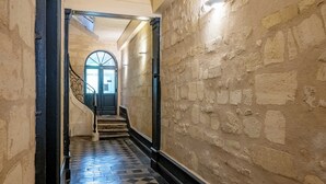 Un corridoio con pavimento a scacchi, una scala con ringhiera nera e un muro in pietra.