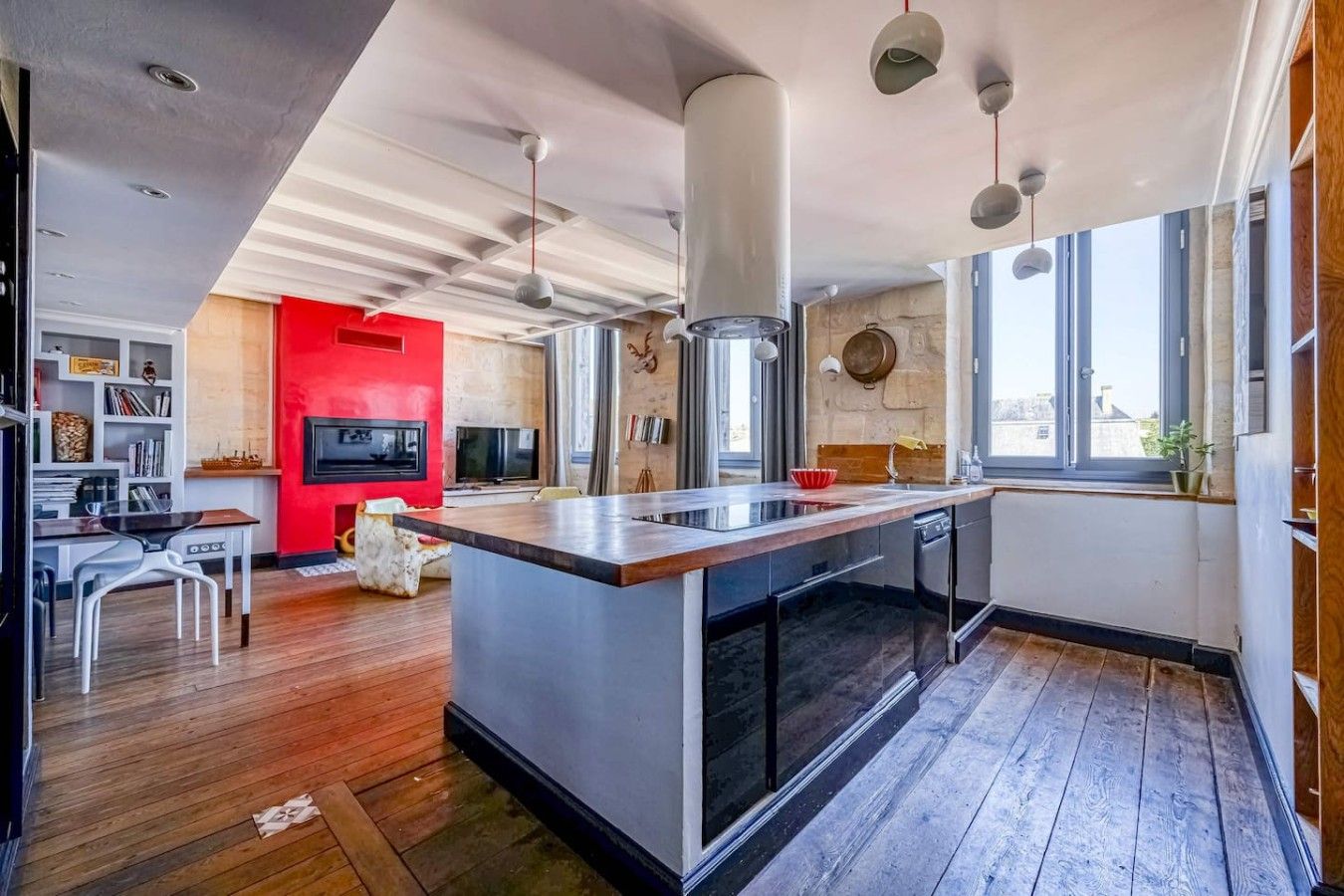 Une cuisine moderne avec un îlot central, un plancher en bois et un mur d’accent rouge.
