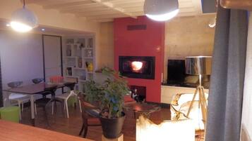 A living room with a fireplace, a dining area with chairs and a table, and a television mounted on the wall.