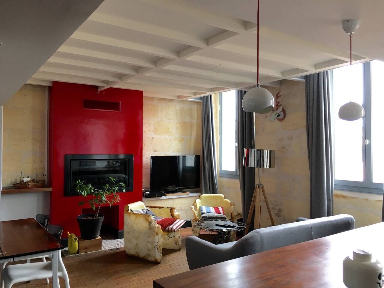 A living room with a red accent wall, a flat-screen TV, a tripod lamp, and a wooden dining table.