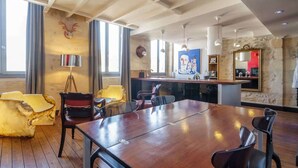 Spaziosa sala da pranzo con un lungo tavolo di legno e diverse sedie, un’area bar con uno specchio e opere d'arte, e un muro in pietra con una testa di animale appesa.