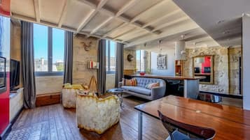 Una sala de estar moderna con piso de madera, un sofá, una mesa de comedor y un ventanal con cortinas.