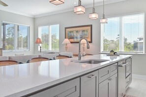 Une cuisine moderne dotée d’un grand îlot central, d’appareils électroménagers en acier inoxydable et offrant une vue sur la ville grâce à de grandes fenêtres.